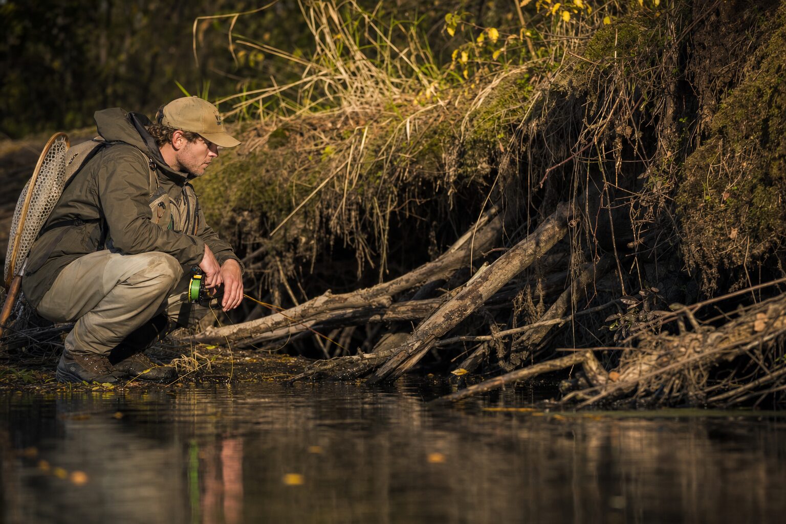 Fly angler crouched beside woody river structure while searching for coastal cutthroat